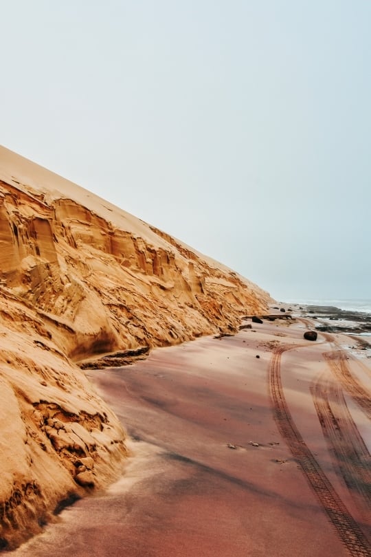 The dramatic meeting point where the high Namib Desert dunes drop directly into the crashing Atlantic Ocean waves.